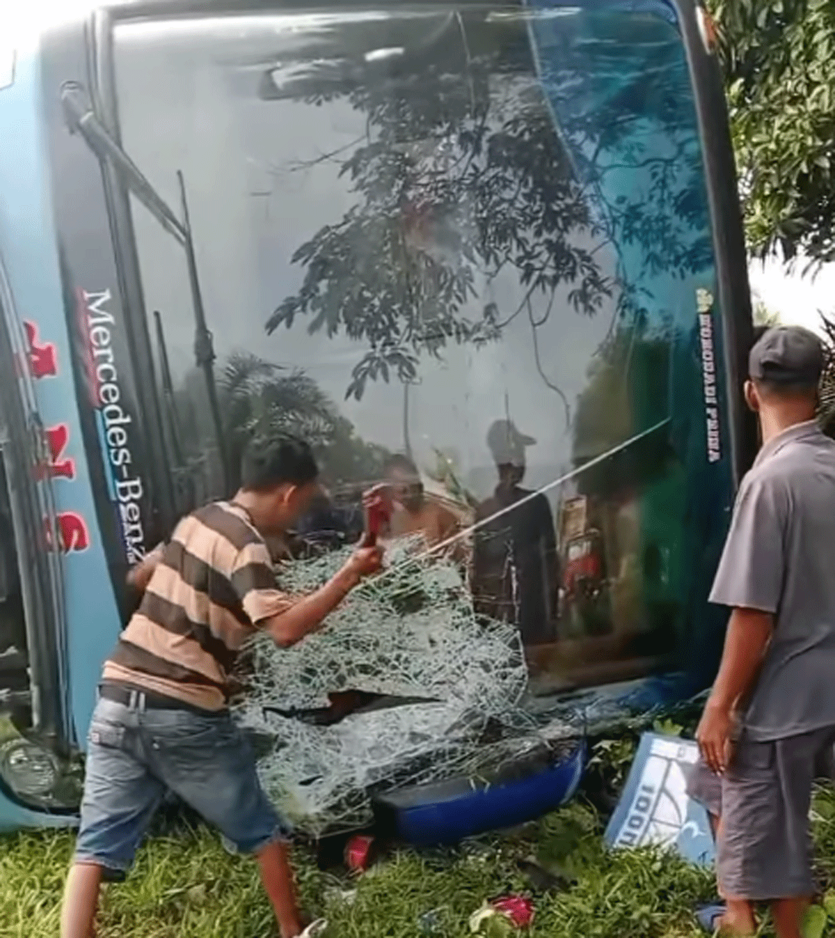 Warga pacahkan kaca depan bus untuk bantu penumpang agar bisa keluar bus yang rebah kuda itu.